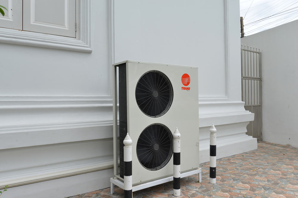 Outdoor air conditioning unit attached to a white wall, featuring two large fans and a Trane logo, surrounded by white and black bollards—exemplifying high-quality HVAC installation.