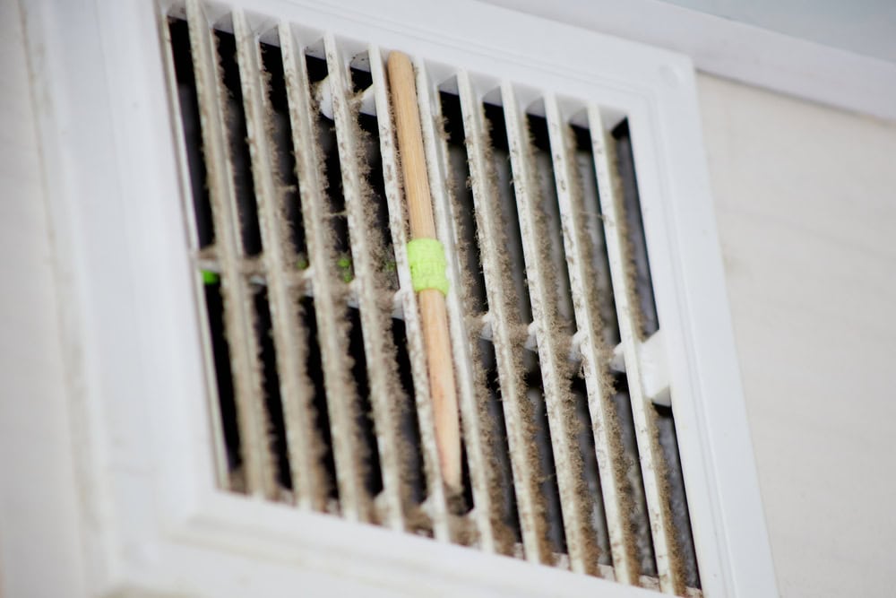 Close-up of a dirty HVAC air vent with a ruler taped in the middle for comparison, highlighting the accumulation of dust and debris, emphasizing the need for regular air duct cleaning.